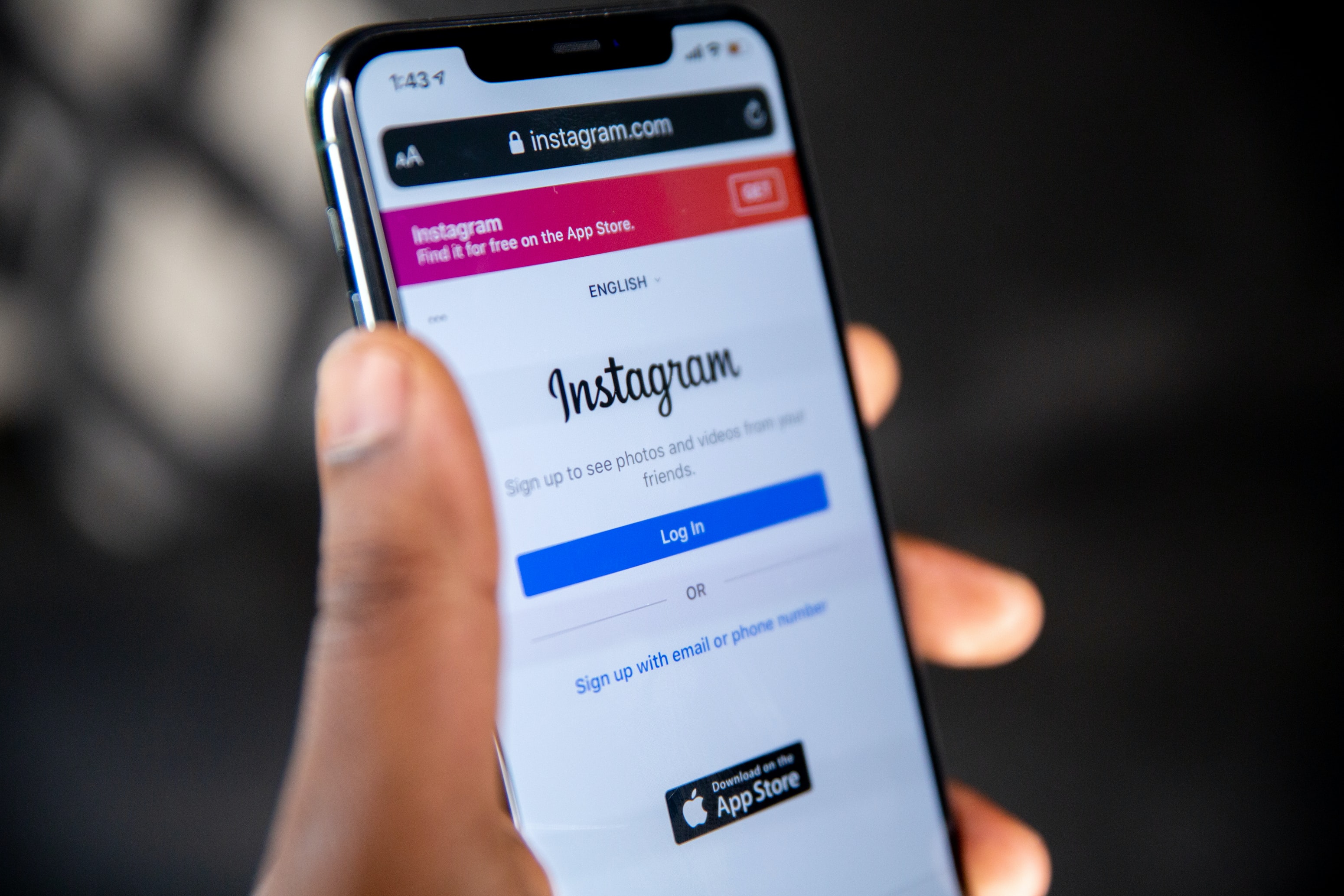Mão de uma pessoa preta segurando um smartphone preto com a tela de login do Instagram aberta.