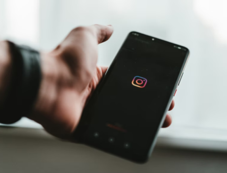 Mão masculina segurando um smartphone com o ícone do Instagram na tela.