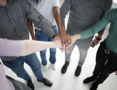 5 people putting their hands together, one on the top of the other.