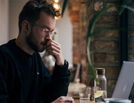 White male in a black jacket making a thoughtful expression while looking at his Macbook.