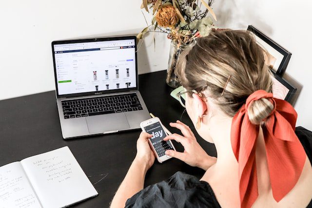 Pessoa editando um story para o Instagram em seu smartphone enquanto navega por um e-commerce em seu notebook.