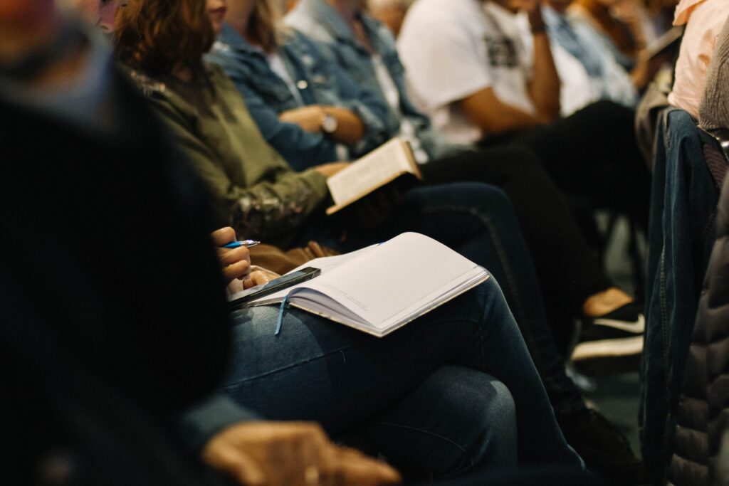 People sitting while watching an event. Everyone has a notebook on their lap where they are writing notes.