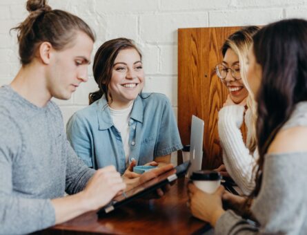 Four people sitting on a table while drinking coffee and chatting.