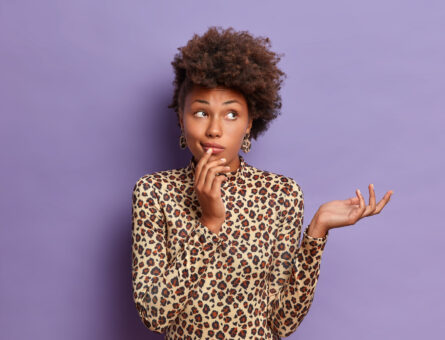woman making a question with a animal print shirt in front of a purple wall